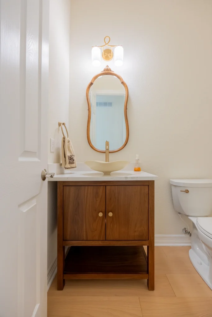 Powder room remodel in Broomfield, CO by Northbuilt Construction featuring a vessel sink, wood vanity, and vintage-style mirror for a warm, transitional look.